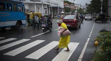 Seorang wanita tua yang mengenakan masker berjalan tanpa alas kaki melalui zebra cross di Kochi, negara bagian Kerala, India, Rabu (6/7/2022). Negara bagian selatan itu telah mewajibkan penggunaan masker di tempat-tempat umum menyusul meningkatnya kasus COVID-19. (AP Photo/ RS Iyer)