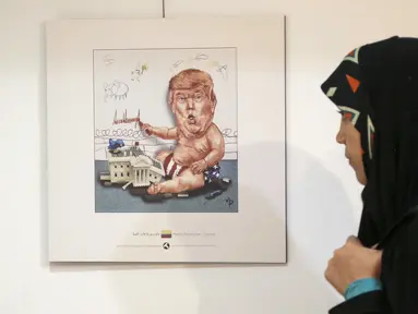 Pengunjung wanita Iran melihat kartun Presiden AS Donald J. Trump di sebuah pameran kartun Trumpisme 2017 Internasional dan kontes karikatur, di ibukota Teheran, Iran (3/7). (AFP Photo/Atta Kenare)