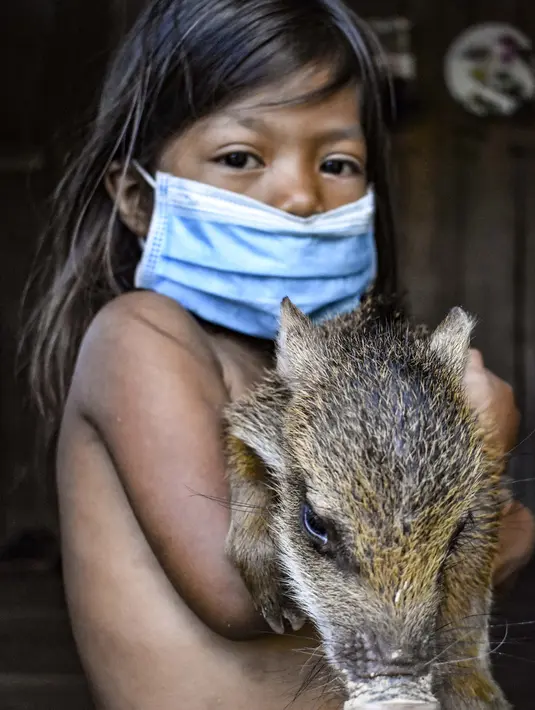 Gadis suku Tikuna berpose mengenakan masker di tengah kekhawatiran virus corona Covid-19 di Leticia, Departemen Amazonas, Kolombia pada 8 Juni 2020. Kasus virus corona ini meningkatkan kekhawatiran akan resiko penyebaran ke masyarakat adat yang rentan dan berada di pedalaman. (Tatiana de NEVO/AFP)