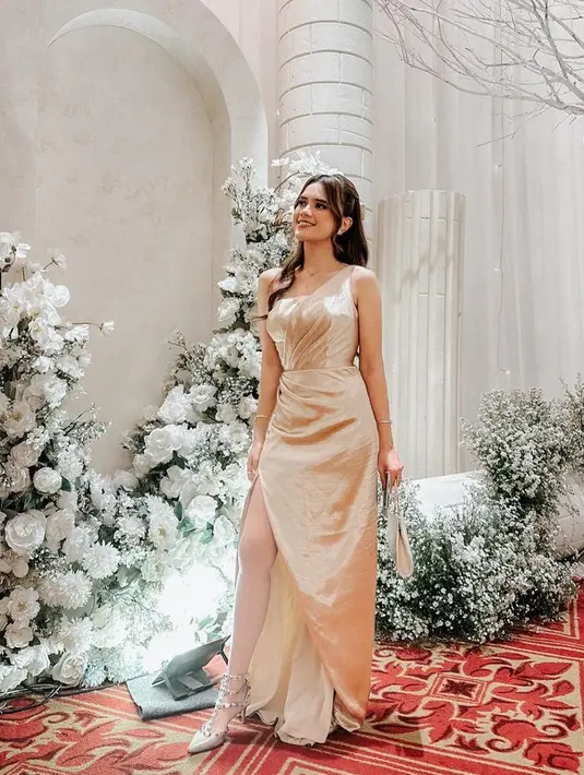 Audi Marissa tampil dengan gaun slit gold dengan model one shoulder. Dipadukan heels dan membawa handbag putih. [@audimarissa]