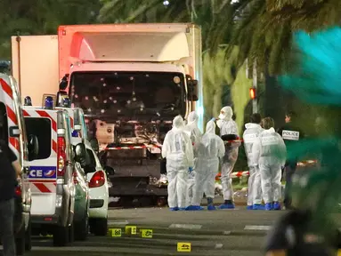 Polisi dan ahli forensik berdiri disamping sebuah truk yang menabrak kerumunan orang yang tengah menyaksikan festival di Nice, Prancis, Kamis (14/7). Sedikitnya 60 orang tewas dan ratusan lainnya luka akibat hantaman truk tersebut. (REUTERS/Eric Gaillard)