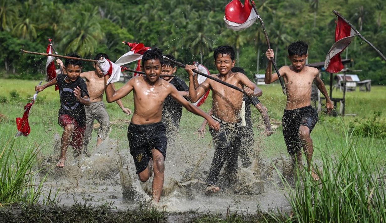 Anak-ana berlari di lapangan sambil membawa bendera Merah Putih saat acara permainan tradisional pada malam Hari Ulang Tahun (HUT) ke-78 Republik Indonesia (RI) di Desa Wisata Nusa, Banda Aceh, Aceh, Rabu (16/8/2023). (CHAIDEER MAHYUDDIN/AFP)
