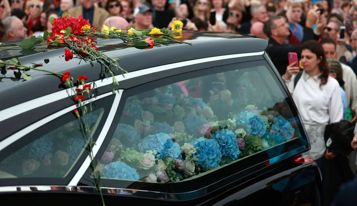 Saat mobil jenazah Sinead O’Connor melaju perlahan, lagu “Natural Mystic” milik Bob Marley pun diputar. Sebagian orang dalam kerumunan itu turut menyanyikan lagu “Natural Mystic” sembari bertepuk tangan, di mana sebagian lainnya sembari mengepalkan tangan sebagai bentuk penghormatan. Sebagian orang lainnya menangis sambil melemparkan bunga ke mobil jenazah yang membawa Sinead O’Connor. (Liam McBurney/PA via AP)