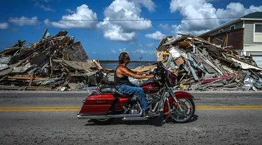 Seorang pengendara sepeda motor melewati puing-puing yang menumpuk dari rumah yang hancur setelah melewati Badai Ian di Pulau Matlacha di Lee County, Florida pada 7 November 2022. Pantai timur Florida berada di bawah pengawasan badai saat negara bagian itu bergulat dengan kehancuran Badai Ian. (AFP/ Giorgio Viera)