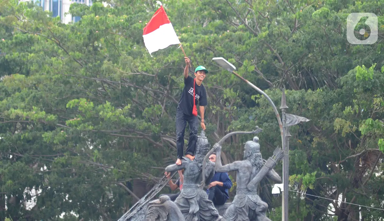 Massa aksi demo tolak omnibus law UU Cipta Kerja naik ke atas patung arjuna wiwaha mengibarkan bendera merah putih di Jalan Medan Merdeka Barat, Jakarta Pusat, Selasa (20/10/2020). (merdeka.com/ Arie Basuki)