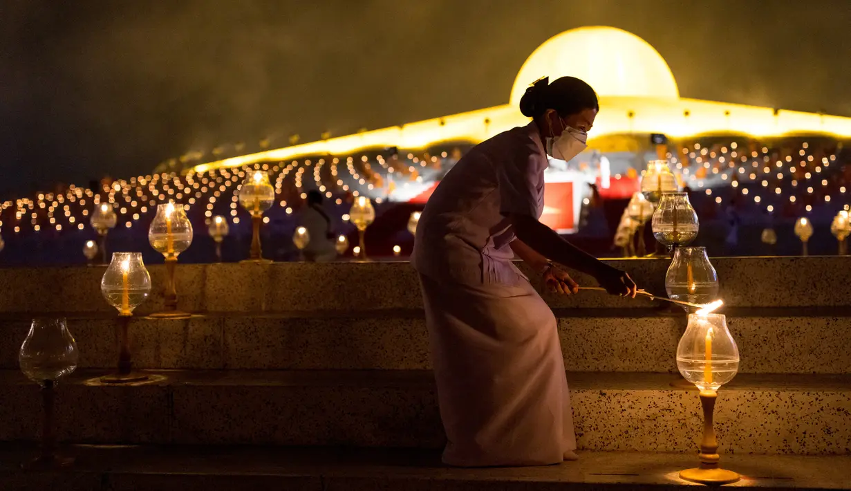 Seorang wanita menyalakan lilin selama perayaan Makha Bucha di kuil Wat Dhammakaya di provinsi Pathum Thani, utara Bangkok (16/2/2022). Hari raya ini dirayakan pada saat bulan purnama di tiap bulan ketiga kalender Buddha. (AFP/Jack Taylor)