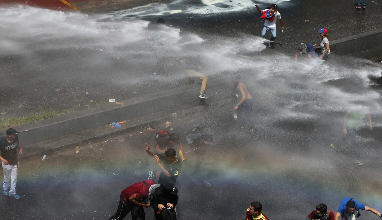 Para demonstran menghindari semprotan water cannon saat bentrok dengan aparat kepolisian di Caracas, Venezuela, (6/4). Banyak yang menilai Keputusan Mahkamah Agung tersebut dinilai sebagai langkah menuju kediktatoran. (AP Photo / Fernando Llano)