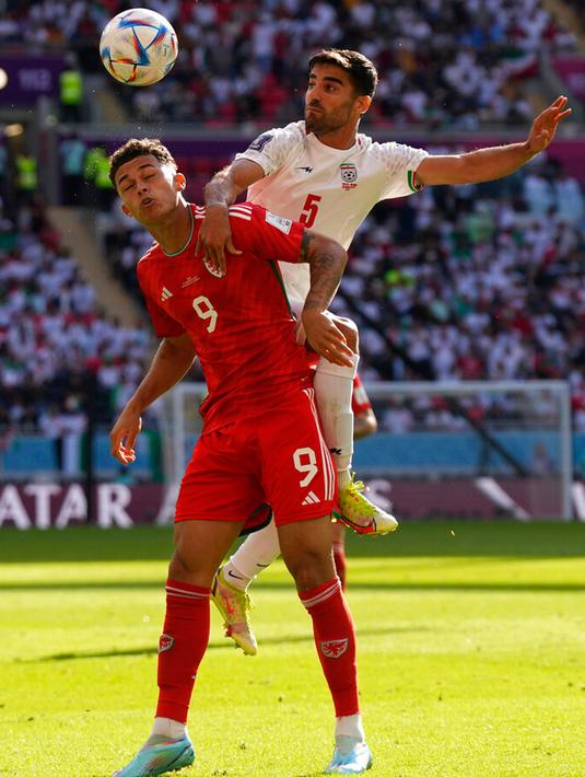 Pemain Wales Brennan Johnson (kiri) berebut bola dengan pemain Iran Milad Mohammadi pada pertandingan sepak bola Grup B Piala Dunia 2022 di Stadion Ahmad Bin Ali, Al Rayyan, Qatar, Jumat (25/11/2022). Iran mengalahkan Wales dengan skor 2-0. (AP Photo/Alessandra Tarantino)
