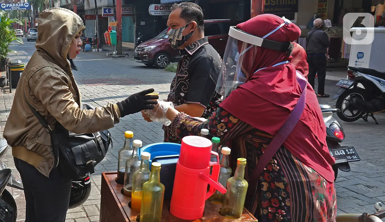 Tidar (46), melayani pembeli di Pasar Baru, Jakarta, Kamis (11/06/2020). Penjual jamu tradisional keliling ini tampak mematuhi protokol kesehatan pencegahan COVID-19 dengan mengenakan masker, face shield, dan sarung tangan dalam melayani pelanggan setianya. (Liputan6.com/Herman Zakharia)