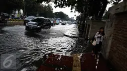 Pejalan kaki melintasi genangan air di kawasan Jalan Merdeka Timur, Jakarta, Selasa (1/11). Hujan deras disertai angin yang mengguyur wilayah Jakarta, mengakibatkan genangan di sejumlah ruas jalan. (Liputan6.com/Faizal Fanani)