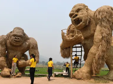 Para siswa berfoto dengan patung King Kong raksasa yang terbuat dari jerami di Huay Teung Tao Lake, Don Kaeo, Chiang Mai, Thailand, Rabu (3/4). Tempat ini merupakan satu dari banyak spot foto instagramable di Chiang Mai. (Lillian SUWANRUMPHA/AFP)