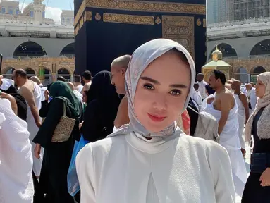 Yuni Shara saat berpose di depan Kakbah. Dia mengenakan gamis putih yang dipadukan dengan hijab bercorak. (Foto: Instagram/ yunishara36)