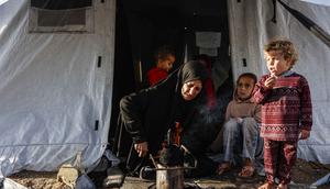 Philippe Lazzarini juga menekankan bahwa bantuan kemanusiaan yang diizinkan masuk saat ini jauh dari skala yang dibutuhkan untuk menangani krisis. Tampak dalam foto, seorang perempuan Palestina memanaskan panci sementara anak-anak memperhatikan di luar tenda tempat tinggalnya saat wilayah tersebut dilanda hujan dan kondisi musim dingin yang dingin, di Kota Gaza pada 28 Desember 2025. (Omar AL-QATTAA/AFP)