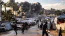 Serangan tersebut memicu kebakaran hebat yang menghanguskan sejumlah tenda pengungsi Palestina di lokasi kejadian. Tampak dalam foto, orang-orang berlarian berlatar kepulan asap hitam setelah serangan udara Israel menghantam sebuah lokasi dekat tenda-tenda penampungan pengungsi Palestina di Deir el-Balah, Jalur Gaza tengah pada 25 Maret 2026. (Eyad Baba/AFP)