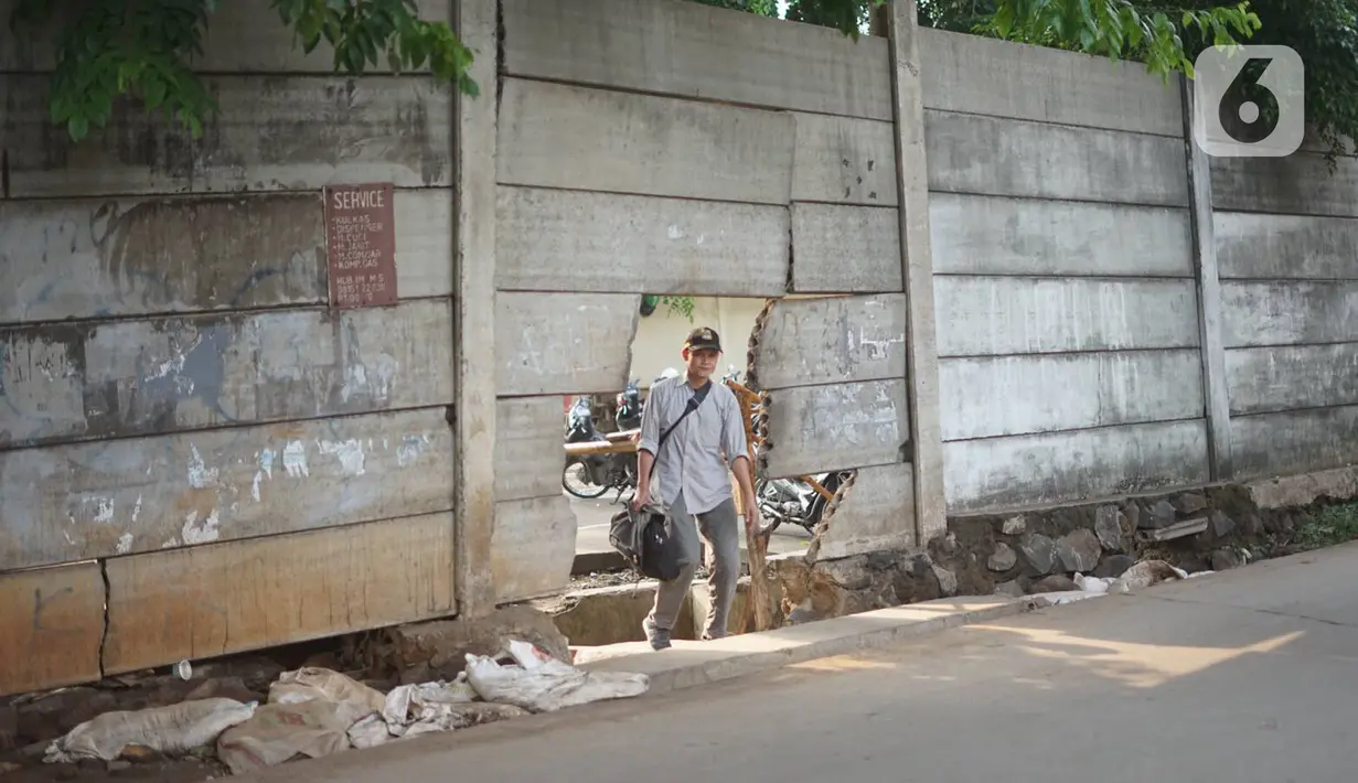 Pejalan kaki melewati tembok berlubang di Terminal Kampung Rambutan, Jakarta, Kamis (19/12/2019). Jauhnya akses bagi pejalan kaki menjadikan tembok berlubang tersebut pintu alternatif untuk keluar dan masuk Terminal Kampung Rambutan. (Liputan6.com/Immanuel Antonius)