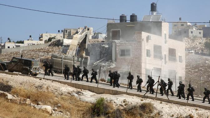 Pasukan keamanan Israel berjaga di tengah penghancuran bangunan Palestina dengan alat berat di Tepi Barat (22/7/2019). Palestina menuduh Israel menggunakan keamanan sebagai dalih untuk mengusir mereka dari Tepi Barat. (AFP Photo/Hazem Bader)