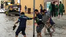 Pemerintah Dubai, UEA, mendesak warga untuk tetap berada di dalam rumah, kecuali jika benar-benar diperlukan. Tampak dalam foto, para pria mengangkat ujung celana mereka untuk menyeberangi genangan air banjir saat melintasi jalan setelah hujan lebat, di Dubai, Uni Emirat Arab (UEA) pada Jumat 19 Desember 2025. (FADEL SENNA/AFP)