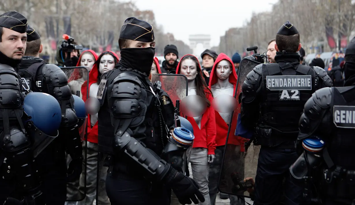 Polisi antihuru-hara menghadang aktivis wanita bertelanjang dada saat aksi protes rompi kuning di Paris, Prancis, Sabtu (15/12). Para aktivis berpakaian seperti Marianne, lambang Republik Perancis. (AP Photo/Kamil Zihnioglu)