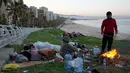 Hingga Jumat 6 Maret 2026, setidaknya ada 26 serangan udara Israel menghantam infrastruktur yang diklaim sebagai milik Hizbullah di Dahiyeh, pinggiran selatan Beirut. Tampak dalam foto, seorang pria pengungsi bersama keluarganya yang melarikan diri dari serangan udara Israel di Dahiyeh, pinggiran selatan Beirut, menyalakan api untuk menghangatkan diri di tepi pantai Beirut, Lebanon, Jumat 6 Maret 2026. (AP Photo/Hussein Malla)