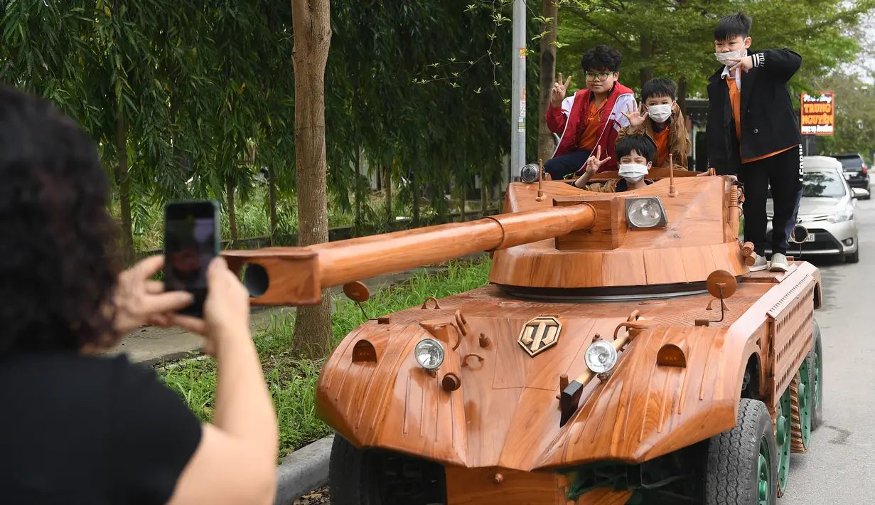 Anak-anak berpose di atas tank kayu di daerah perumahan di provinsi Bac Ninh, Vietnam pada 28 Maret 2022. Kendaraan kayu, berdasarkan model EBR105 Prancis dan lengkap dengan meriam replika sepanjang 2,8 meter itu, menghabiskan dana USD11 ribu atau sekitar Rp158 juta. (Nhac NGUYEN /AFP)