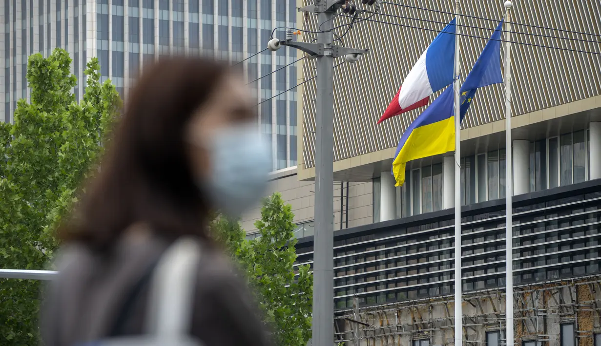 Seseorang yang memakai masker menunggu untuk melintasi persimpangan saat bendera Prancis, Ukraina, dan Uni Eropa berkibar di Kedutaan Besar Prancis di Beijing, China, Rabu (17/5/2023). (AP Photo/Mark Schiefelbein)
