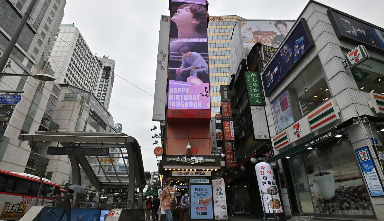 Seorang perempuan melewati layar listrik besar bergambar personel boyband BTS, Jeon Jung-kook, di sebuah distrik perbelanjaan di Seoul, Selasa (1/9/2020). Bangtan Boys (BTS) menjadi artis Korea Selatan pertama yang berhasil menempati puncak Billboard Hot 100 dengan lagu Dynamite. (Jung Yeon-je/AFP)