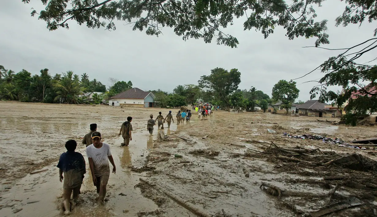 Penduduk desa berjalan melalui daerah banjir di desa Radda di Kabupaten Luwu Utara, Sulawesi Selatan (14/7/2020). Akibat musibah banjir bandang ini setidaknya sekitar 15 orang tewas dan belasan lainnya dinyatakan hilang. (AP Photo)