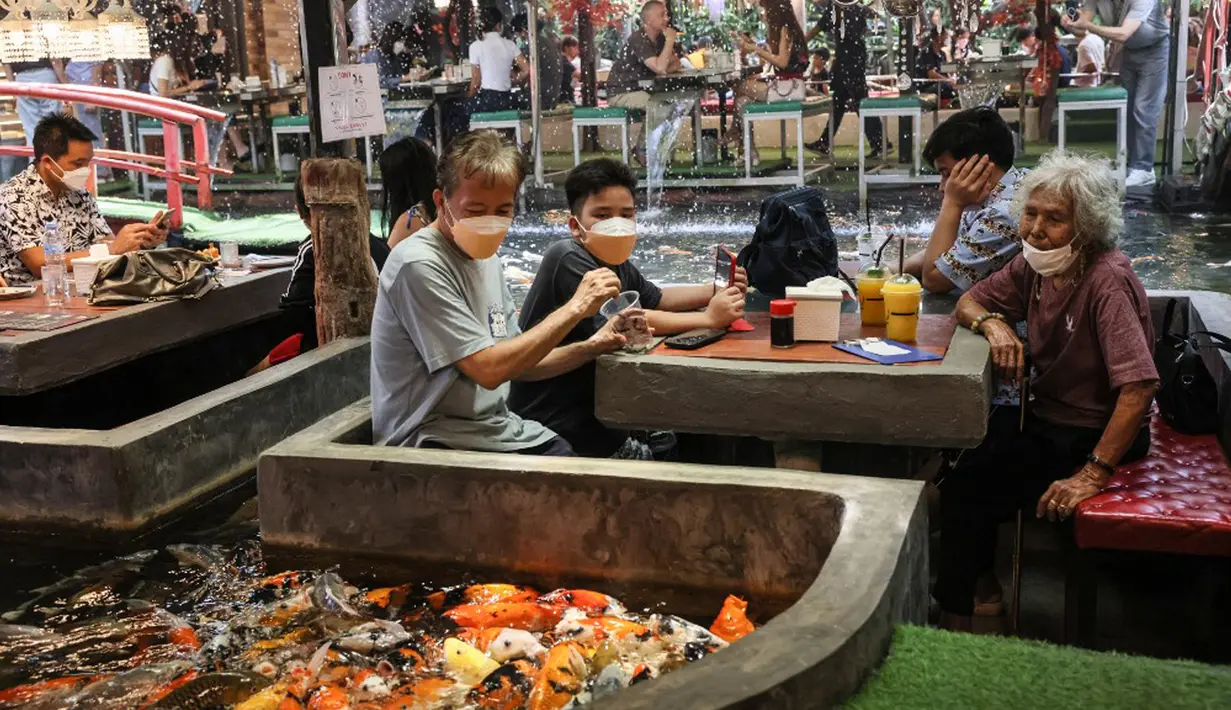 Pengunjung memberi makan ikan mas di restoran bertema ikan di Chiang Mai, Thailand, Selasa (12/4/2022). (Jack TAYLOR/AFP)