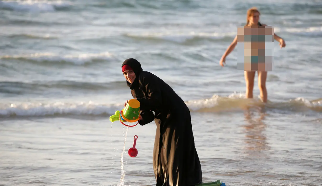 Seorang wanita muslim bermain di Pantai Laut Mediterania, Tel Aviv, Israel pada 22 Agustus 2016. Saat pengunjung pantai mengenakan busana yang minim mereka tetap mengenakan jilbab dan busananya. (REUTERS / Baz Ratner)