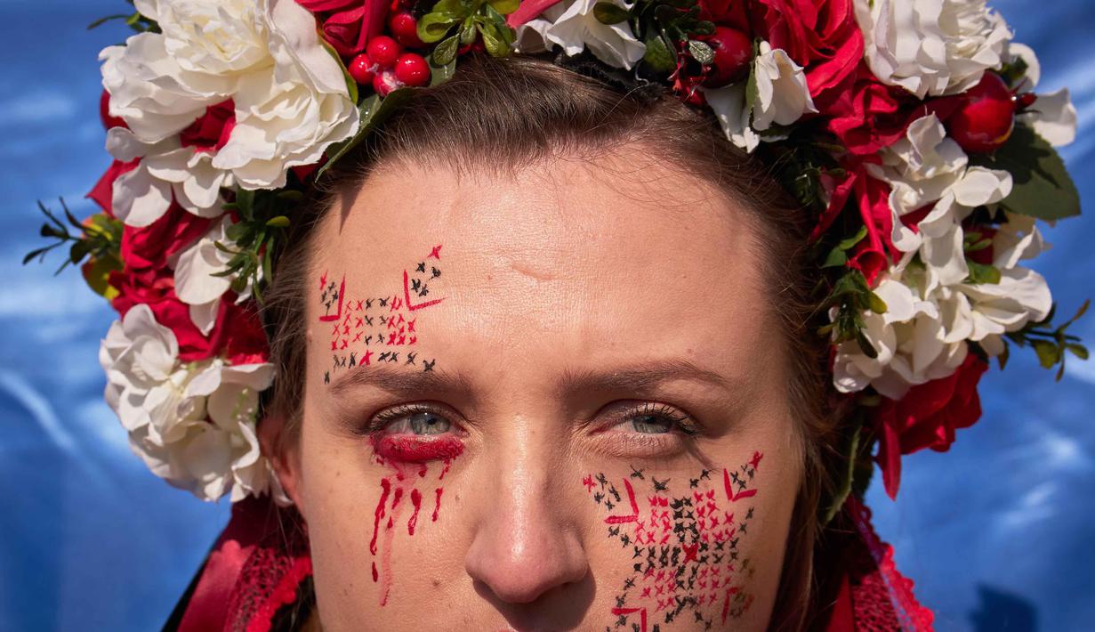 Mereka mengecam agresi militer Rusia, dan menyerukan penghentian perang. Tampak dalam foto, seorang wanita mengenakan mahkota bunga saat anggota komunitas Ukraina menggelar protes untuk menandai tahun keempat sejak dimulainya invasi skala penuh Rusia ke Ukraina di Bukares, Rumania, Minggu 22 Februari 2026. (AP Photo/Vadim Ghirda)