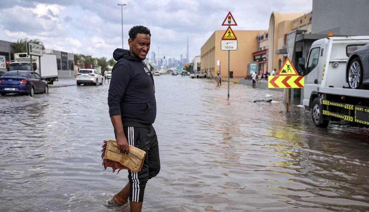Pengumuman ditegaskan bertujuan menjaga keselamatan warga. Tampak dalam foto, seorang pria menerobos genangan air banjir setelah hujan lebat di Dubai, Uni Emirat Arab (UEA) pada Jumat 19 Desember 2025. (FADEL SENNA/AFP)