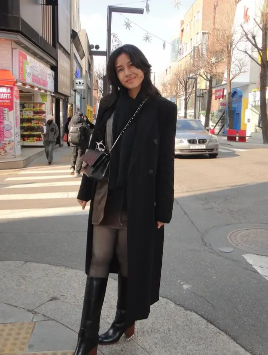 Bagian bawah outfit Shenina semakin standout berkat kombinasi rok mini, sheer tights, dan knee-high boots hitam dengan heels kayu yang kokoh.
