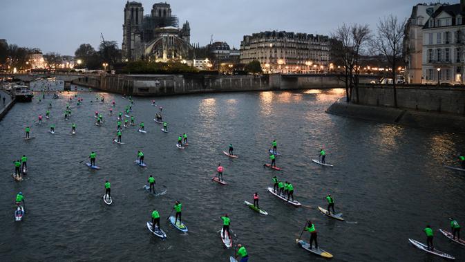 Para peserta Nautic Paddle Race atau lomba dayung sambil berdiri melintas dekat Katedral Notre-Dame di Paris, Minggu (8/12/2019). Sekitar 1000 pesaing ikut serta dalam lomba sejauh 11 kilometer menyeberangi sungai Seine dengan pemandangan kota Paris. (Photo by Olivier MORIN / AFP)