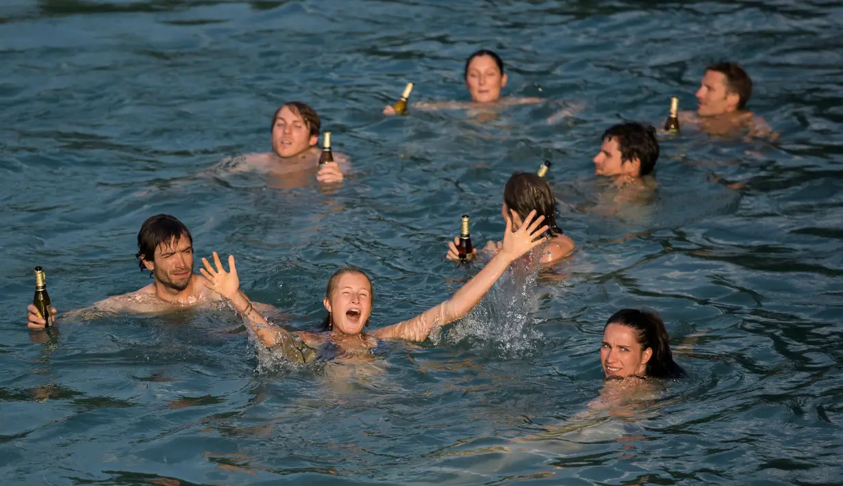<p>Sekelompok anak muda membawa bir saat berenang di Sungai Aare, Bern, Swiss, 21 Juni 2017. Sungai Aare memiliki lebar yang bervariasi mulai dari 40 meter, 100 meter, bahkan satu titik dekat pintu pembangkit listrik tenaga air Muhlenberg lebarnya bisa mencapai 647,65 meter. (Fabrice COFFRINI/AFP)</p>