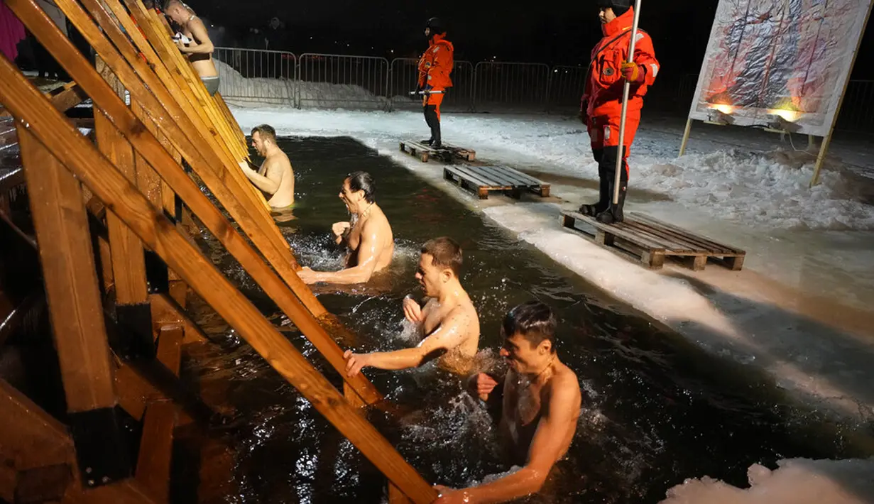 Petugas penyelamat mengamati penganut Kristen Ortodoks Rusia berendam dalam air es saat perayaan Epiphany tradisional di St. Petersburg, Rusia, 19 Januari 2022. Ribuan penganut Kristen Ortodoks Rusia merayakan Epiphany dengan membenamkan diri dalam air dingin. (AP Photo/Dmitri Lovetsky)