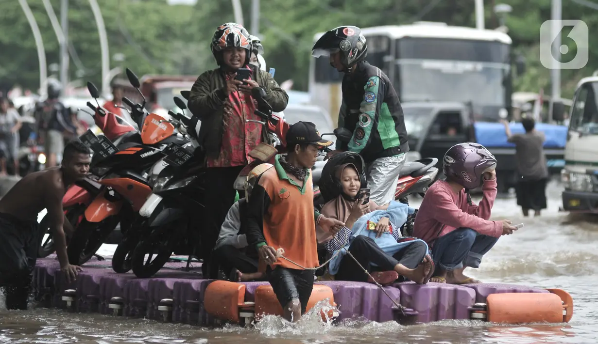 Pengendara sepeda motor menggunakan jasa rakit saat banjir melanda Cempaka Putih, Jakarta, Minggu (23/2/2020). Pengendara memanfaatkan jasa angkutan rakit yang ditawarkan warga agar dapat melewati banjir. (merdeka.com/Iqbal S. Nugroho)
