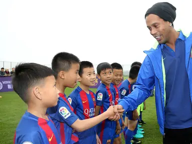 Mantan pemain Barcelona, Ronaldinho, menyalami anak-anak saat peluncuran akademi sepak bola Barcelona di China, Jumat (24/2/2017). (AFP/Handout)