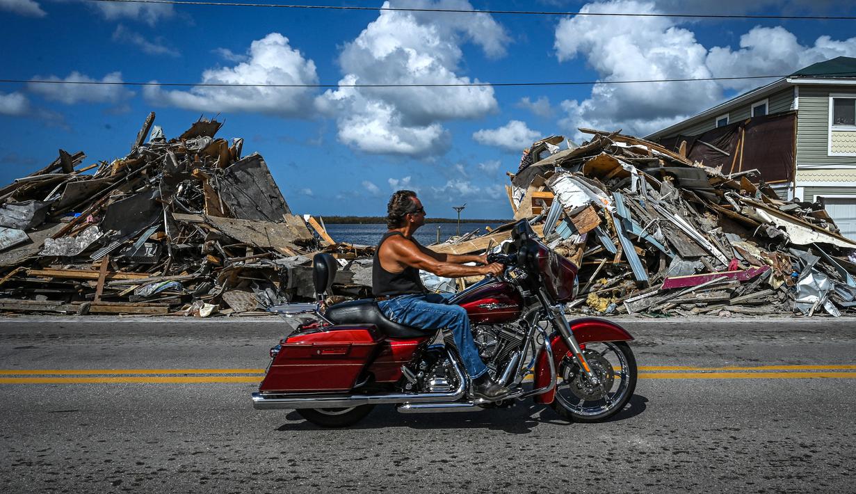 Seorang pengendara sepeda motor melewati puing-puing yang menumpuk dari rumah yang hancur setelah melewati Badai Ian di Pulau Matlacha di Lee County, Florida pada 7 November 2022. Pantai timur Florida berada di bawah pengawasan badai saat negara bagian itu bergulat dengan kehancuran Badai Ian. (AFP/ Giorgio Viera)