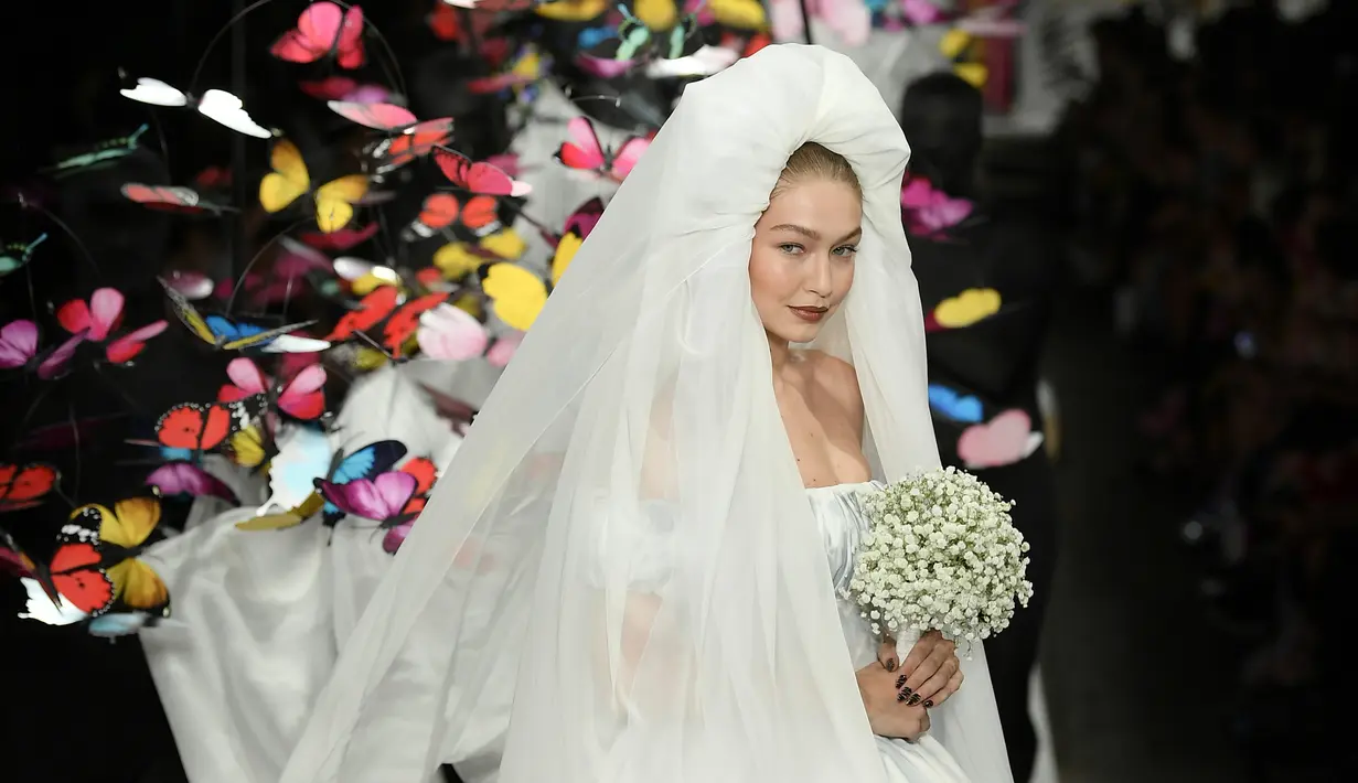 Gigi Hadid berjalan di runway mengenakan gaun rumah mode Moschino untuk koleksi SS19 selama gelaran fashion week di Milan, Italia, Kamis (20/9). Dilengkapi dengan veil berbahan tulle, Gigi Hadid berjalan menggenggam buket bunga. (AFP/Marco BERTORELLO)