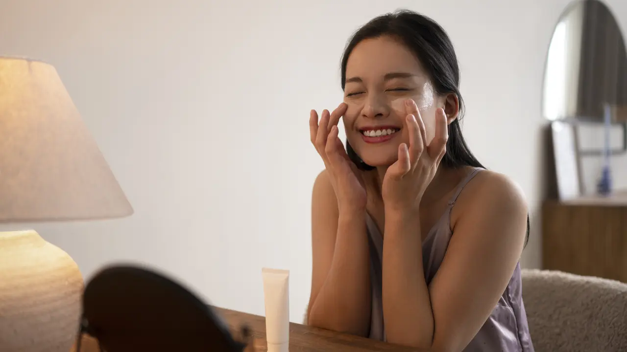 Seorang perempuan sedang mengenakan krim wajah sambil berbermin (Foto Dok: Freepik/freepik)