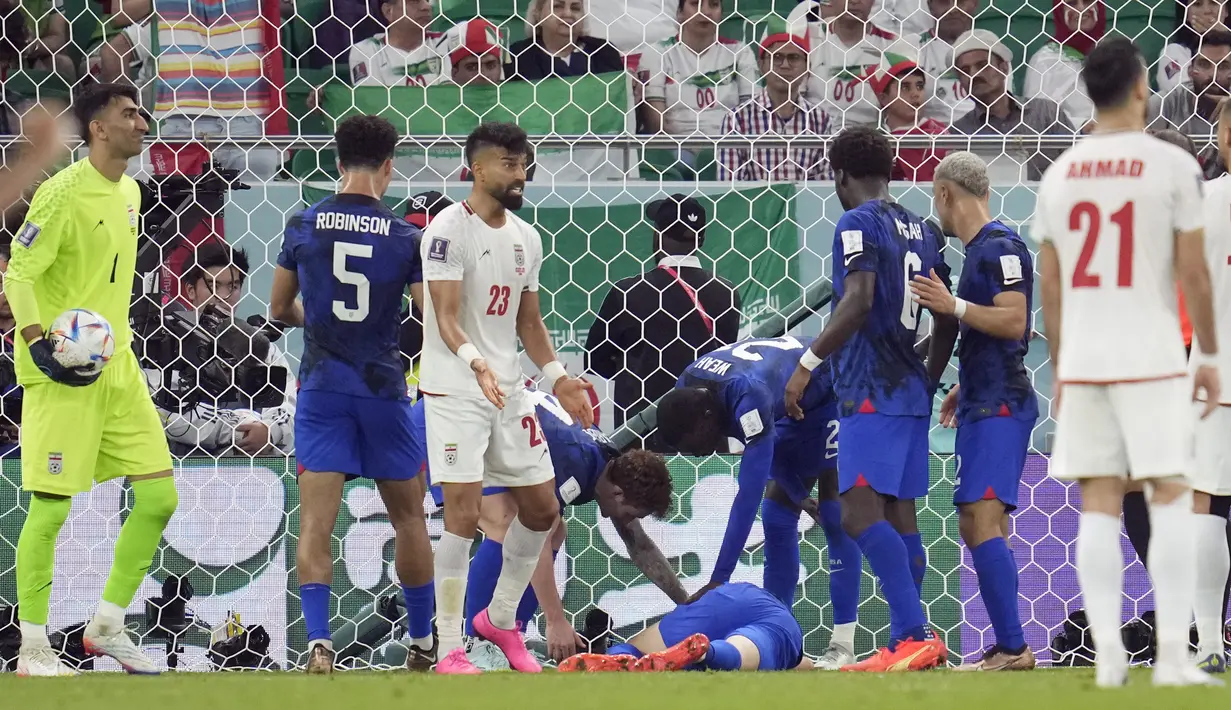 Gelandang Amerika Serikat Christian Pulisic berbaring di lapangan karena cedera saat rekan satu timnya memeriksanya pada laga pamungkas Grup B Piala Dunia 2022 kontra Iran di Stadion Al Thumama, Rabu (30/11/2022) dini hari WIB. Setelah beberapa menit menjalani perawatan, Pulisic ditarik keluar saat turun minum.  (AP Photo/Ashley Landis)