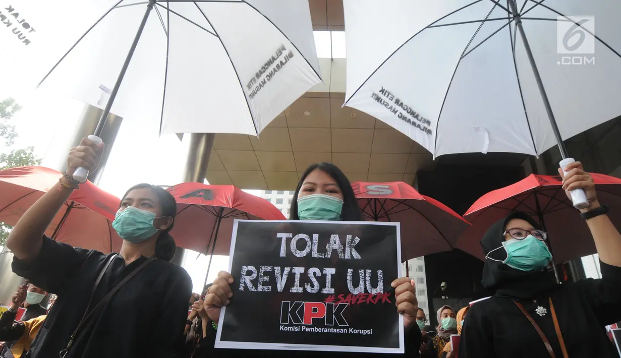 Pegawai KPK membawa poster saat menggelar aksi di Lobi Gedung KPK, Kuningan, Jakarta, Jumat (6/9/2019). Dalam aksi menolak revisi UU KPK tersebut, mereka mengenakan baju serba hitam lengkap dengan masker penutup mulut dan membawa payung. (merdeka.com/Dwi Narwoko)