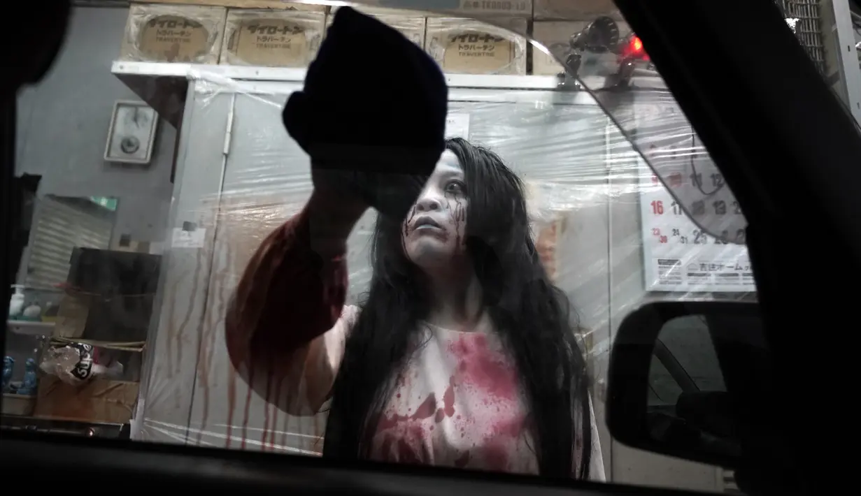 Pemeran zombie membersihkan darah palsu pada kendaraan saat demonstrasi pertunjukan rumah hantu drive-in di Tokyo, Jepang, Selasa (18/8/2020). Rumah hantu drive-in ini diadakan di tengah pandemi COVID-19. (AP Photo/Eugene Hoshiko)