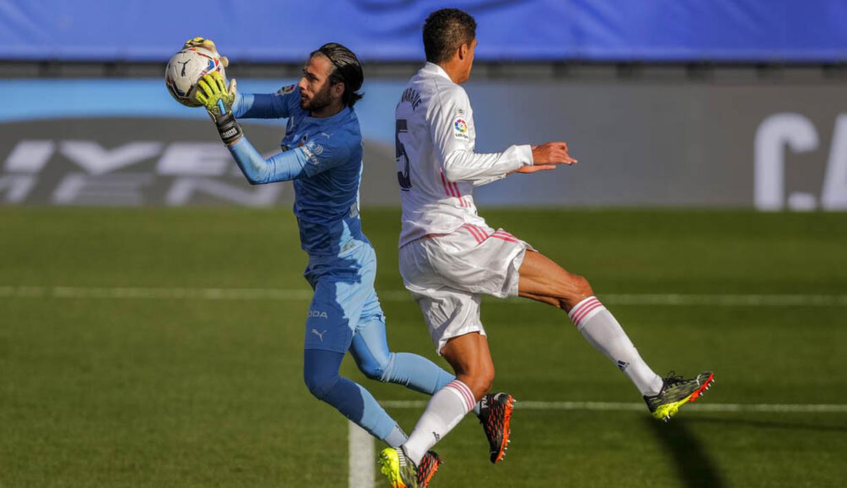 Bek Real Madrid, Raphael Varane, berebut bola dengan kiper Valencia, Jaume Domenech, pada laga Liga Spanyol di Stadion Alfredo Di Stefano, Minggu (14/2/2021). Real Madrid menang dengan skor 2-0. (AP/Manu Fernandez)