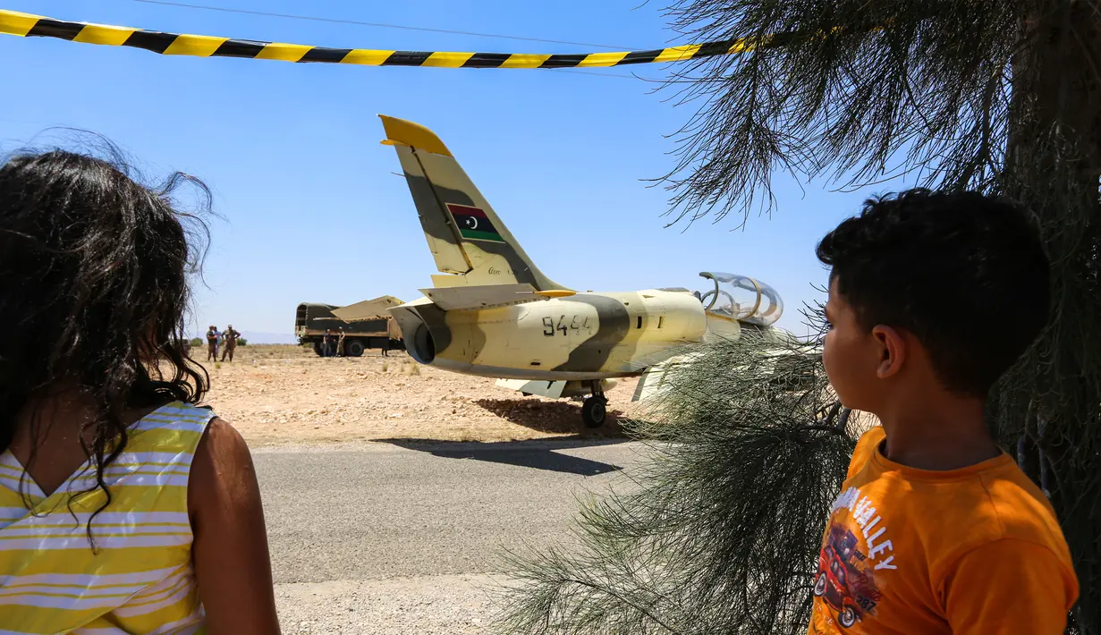 Dua anak melihat kondisi pesawat jet tempur Libya L-39 Albatros pasukan Khalifa Haftar di Kota Medenine di perbatasan Tunisia-Libya (22/7/2019). Jet tempur yang sedang melakukan misi pengintaian dan patroli itu mengalami masalah teknis yang mengakibatkan pendaratan darurat di jalan raya. (AFP Photo/