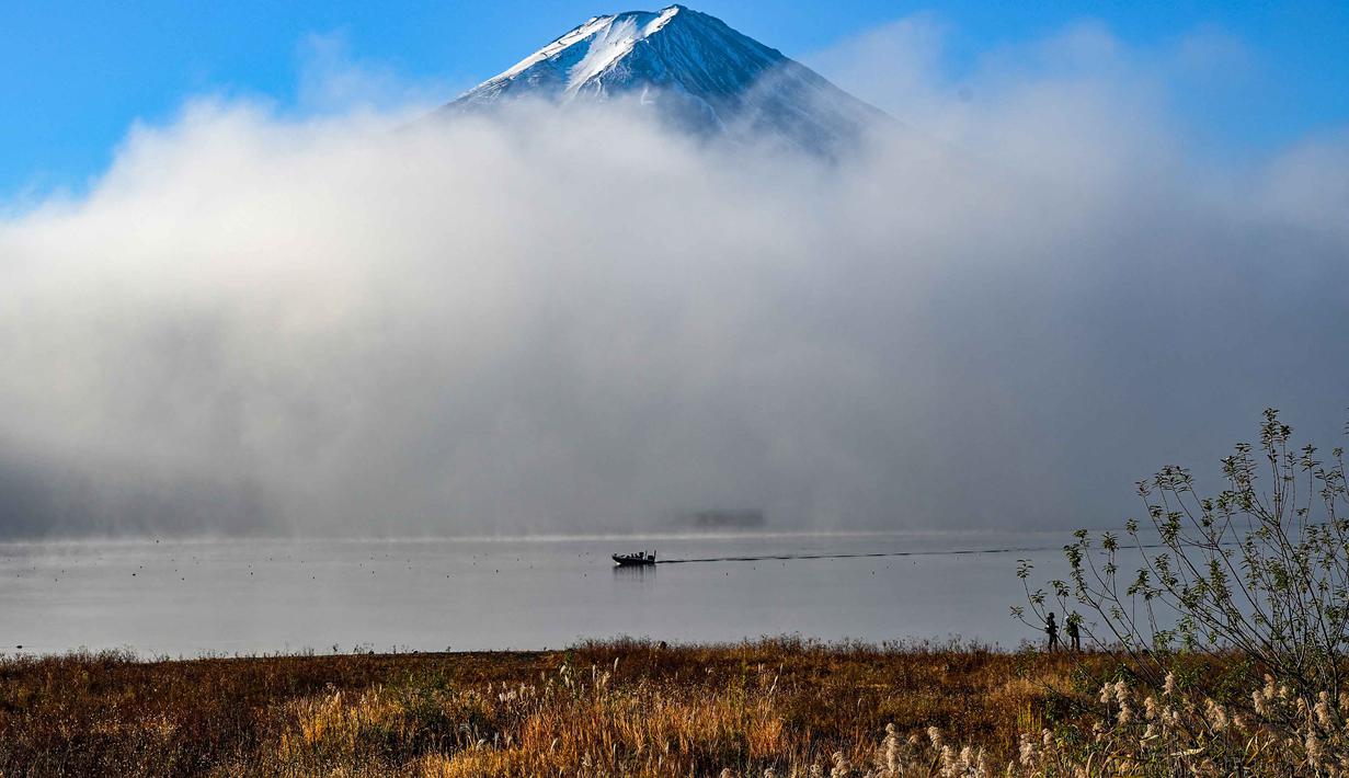 Pengunjung dapat menikmati keindahan Gunung Fuji dari berbagai sudut pandang di sekitarnya, seperti dari area Danau Kawaguchiko atau saat menaiki Shinkansen (kereta cepat) antara Tokyo dan Kyoto. Tampak dalam foto, Gunung Fuji, gunung tertinggi di Jepang dengan ketinggian 3.776 meter (12.460 kaki), terlihat dari kota Fujikawaguchiko, Prefektur Yamanashi pada Senin 17 November 2025 pagi hari. (Caroline GARDIN/AFP)