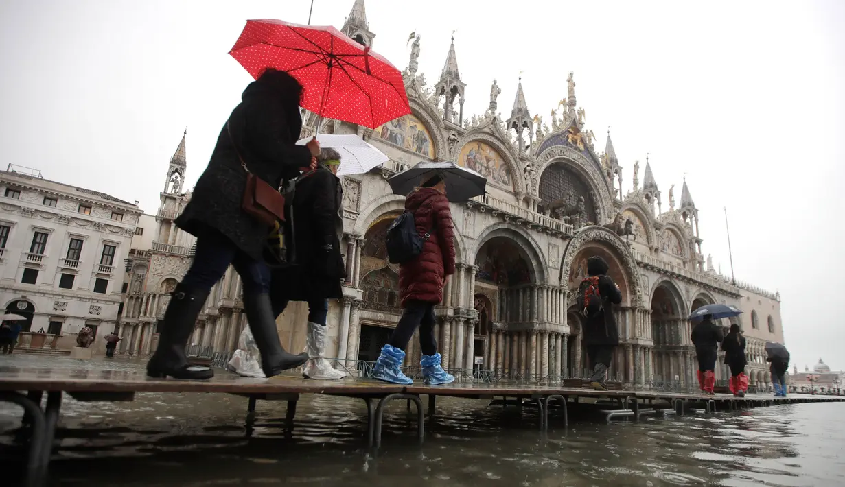 Sejumlah warga berjalan melewati papan saat gelombang pasang membuat banjir depan Basilika Santo Markus, Venesia, Italia, Selasa (12/11/2019). Venesia dilanda banjir akibat gelombang pasang setinggi 127 cm. (AP Photo/Luca Bruno)