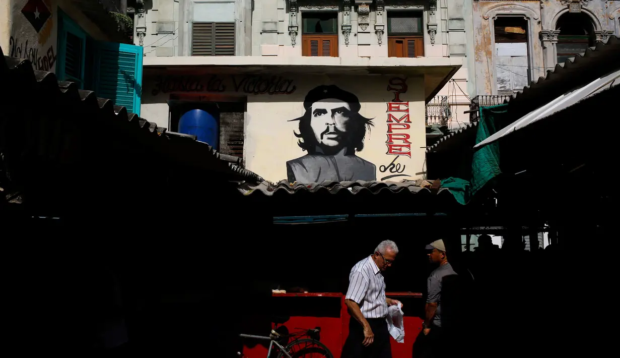 Warga beraktivitas di bawah sebuah mural pahlawan Revolusi Kuba Ernesto 'Che' Guevara yang menghadap ke pasar makanan di Havana, Kuba (28/12). Havana adalah kota terbesar di Kuba dan di seluruh Karibia. (AP Photo / Desmond Boylan)