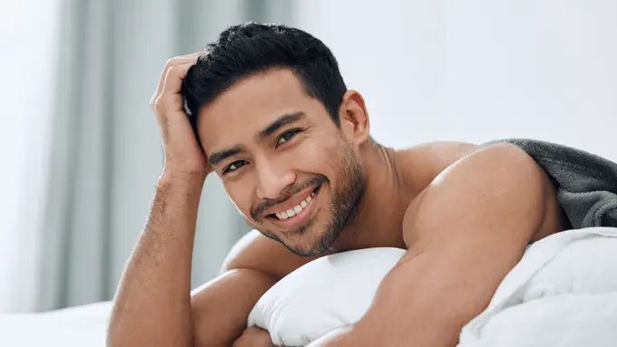 pria tersenyum manis di tempat tidur