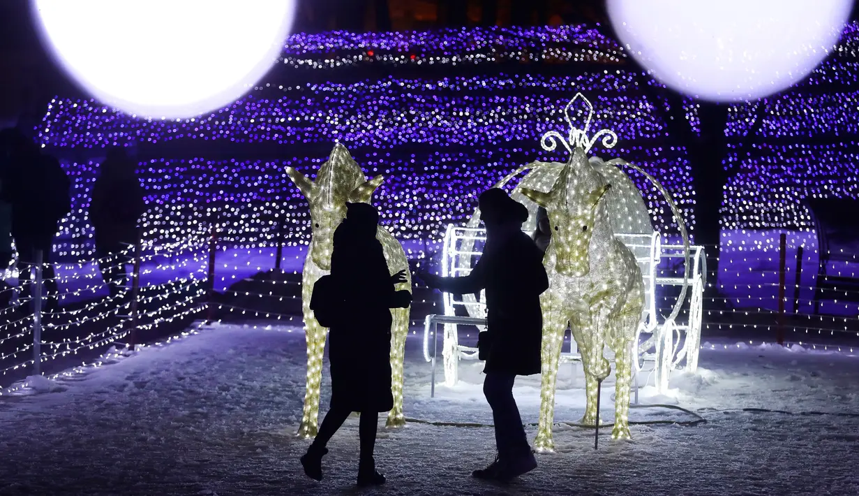 Dua wanita melihat cahaya berbentuk kuda di taman di Minsk, Belarus (28/12). Setelah matahari terbenam, orang-orang berdatangan untuk menikmati pameran cahaya lampu yang dipasang di seluruh taman. (AP Photo/Grits Sergei)